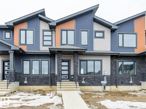 The property showcases a modern architectural design with a multi-toned exterior, featuring dark grey stonework, blue and tan siding, and black framed windows - 3828 38 Street E, Beaumont, AB - Outdoor With Facade
