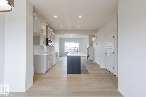 The kitchen features light-toned cabinetry with dark hardware, a white subway tile backsplash, and a central island with a sink and dark base - 3828 38 Street E, Beaumont, AB - Indoor Photo Showing Kitchen