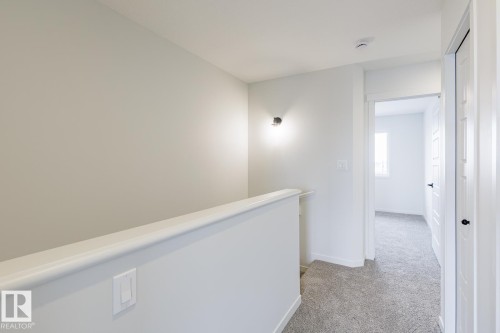 Bright landing area featuring light grey walls, a modern wall sconce, and grey carpeted flooring - 3828 38 Street E, Beaumont, AB - Indoor Photo Showing Other Room