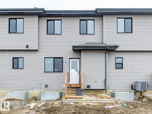 The property features light gray horizontal siding, black-framed windows, and a white exterior door with a small overhang - 3828 38 Street E, Beaumont, AB - Outdoor With Exterior