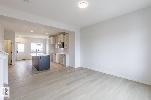 Open concept living space featuring light-toned flooring, a kitchen island with a sink, white cabinetry, and a microwave - 3828 38 Street E, Beaumont, AB - Indoor Photo Showing Kitchen