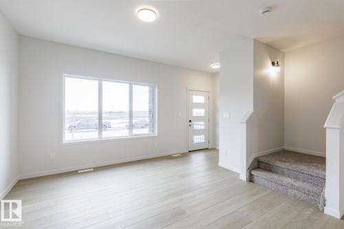 The property features an entryway with light wood flooring, a window offering views of the outdoors, and a staircase with carpeted steps - 3828 38 Street E, Beaumont, AB - Indoor Photo Showing Other Room