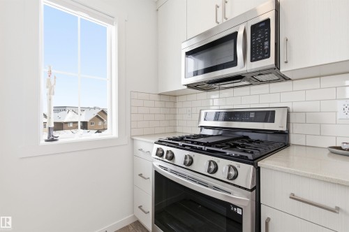 The kitchen features a stainless steel oven and microwave, white cabinetry, a light-colored countertop, and a white subway tile backsplash - 58 1110 Daniels Link Link, Edmonton, AB - Indoor Photo Showing Kitchen