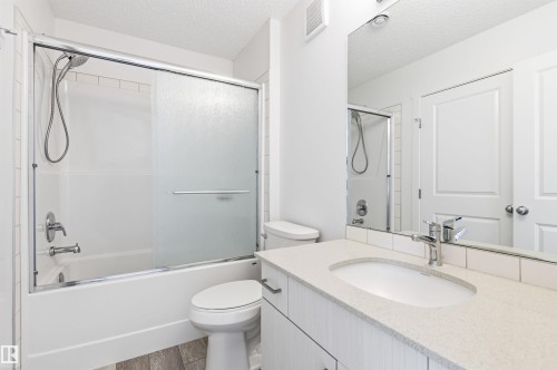 Bathroom featuring a modern vanity with a rectangular sink and a polished chrome faucet, a tub with a sliding glass shower door, and subway tile surround - 58 1110 Daniels Link Link, Edmonton, AB - Indoor Photo Showing Bathroom