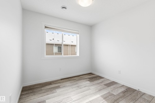 This room features light-colored walls, a window with white trim, and wood-look flooring - 58 1110 Daniels Link Link, Edmonton, AB - Indoor Photo Showing Other Room