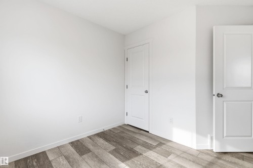 This room features light-colored walls, wood-style flooring, and two white paneled doors - 58 1110 Daniels Link Link, Edmonton, AB - Indoor Photo Showing Other Room