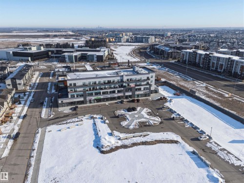 The property is a modern building with a flat roof, featuring balconies and ground-floor retail spaces, situated with surrounding roads and parking areas - 58 1110 Daniels Link Link, Edmonton, AB - Outdoor With View