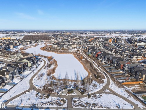 The property is situated within a community featuring a frozen lake, surrounded by pathways, and residential homes - 58 1110 Daniels Link Link, Edmonton, AB - Outdoor With View