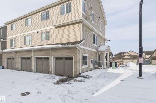 The property features a three-story exterior with horizontal siding, multiple windows, and individual garage doors - 58 1110 Daniels Link Link, Edmonton, AB - Outdoor