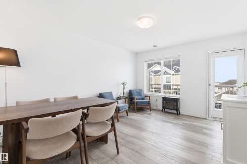 This open-concept living area features light wood-look flooring, ample natural light from a large window, and a glass-paneled exterior door - 58 1110 Daniels Link Link, Edmonton, AB - Indoor Photo Showing Dining Room