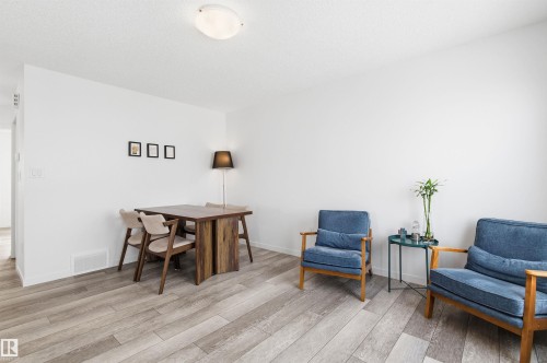 Living area featuring wood-style flooring, a dining space with a dark wood table, and an inviting seating area with two blue upholstered armchairs - 58 1110 Daniels Link Link, Edmonton, AB - Indoor