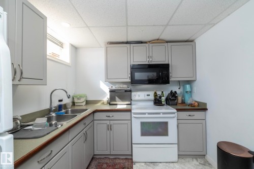 The kitchen features light gray cabinetry, a double basin stainless steel sink, and white appliances including a range - 12 Mill Drive, St. Albert, AB - Indoor Photo Showing Kitchen With Double Sink