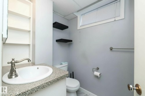 The bathroom features a white sink with a classic-style brushed nickel faucet, a speckled countertop, and a built-in shelving unit - 12 Mill Drive, St. Albert, AB - Indoor Photo Showing Bathroom