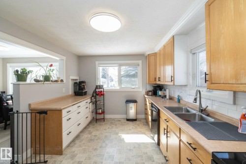 The kitchen features abundant light wooden cabinetry, a double basin stainless steel sink, and light-colored countertops - 12 Mill Drive, St. Albert, AB - Indoor Photo Showing Kitchen With Double Sink