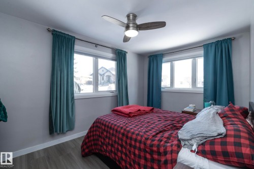 This bedroom features two windows, a ceiling fan with integrated lighting, and light-toned flooring - 12 Mill Drive, St. Albert, AB - Indoor Photo Showing Bedroom