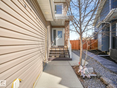 The property features a front entrance with steps leading to a white door, framed by stone accents and light-colored siding - 3910 49 Avenue, Beaumont, AB - Outdoor