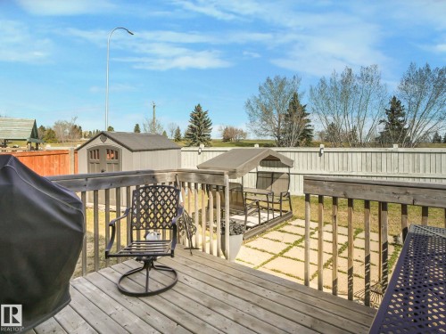 The property features a wooden deck with a railing, overlooking a yard with a storage shed and a white privacy fence - 3910 49 Avenue, Beaumont, AB - Outdoor With Deck Patio Veranda