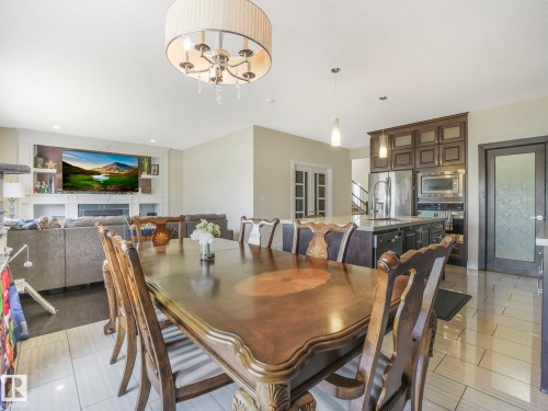 Spacious open concept living area featuring a dining area with tile flooring, a kitchen with dark cabinetry and stainless steel appliances, and a living room with a fireplace and built-in shelving - 3910 49 Avenue, Beaumont, AB - Indoor Photo Showing Dining Room