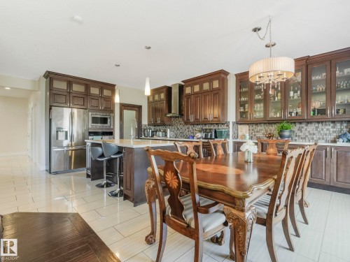 The kitchen and dining area features abundant dark wood cabinetry, stainless steel appliances, a kitchen island with seating, and light-toned tile flooring - 3910 49 Avenue, Beaumont, AB - Indoor Photo Showing Dining Room