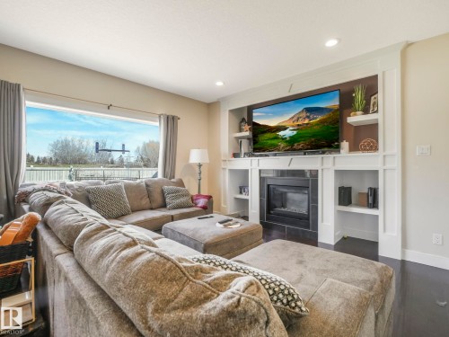Living area with a large window, recessed lighting, and a fireplace featuring a dark tile surround and built-in shelving - 3910 49 Avenue, Beaumont, AB - Indoor Photo Showing Living Room With Fireplace