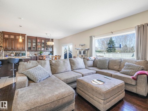 Living area with dark hardwood flooring, a large window providing views of outdoor trees and a fence, and a sliding glass door leading to the exterior - 3910 49 Avenue, Beaumont, AB - Indoor Photo Showing Living Room