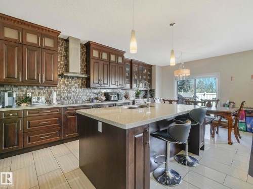 The kitchen features dark wood cabinetry, a mosaic tile backsplash, and a central island with a light-colored countertop - 3910 49 Avenue, Beaumont, AB - Indoor Photo Showing Kitchen With Upgraded Kitchen
