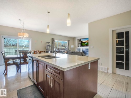 Open concept living area featuring a kitchen island with a double sink and ample cabinetry, light-colored countertops, and tiled flooring - 3910 49 Avenue, Beaumont, AB - Indoor Photo Showing Kitchen With Double Sink
