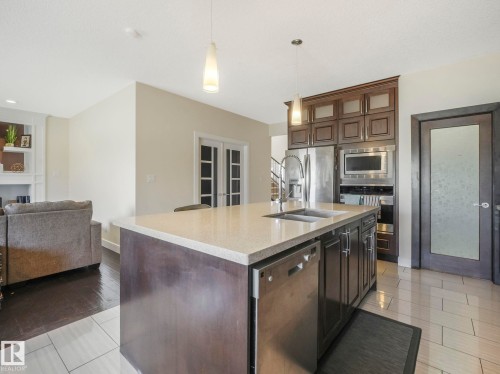 The kitchen features a large island with a sink and a light-toned countertop, dark wood cabinetry, and stainless steel appliances - 3910 49 Avenue, Beaumont, AB - Indoor Photo Showing Kitchen With Stainless Steel Kitchen With Double Sink With Upgraded Kitchen