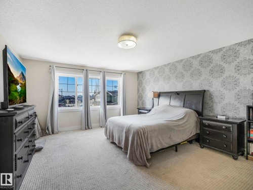 This bedroom features patterned wallpaper, a carpeted floor, and three windows providing natural light - 3910 49 Avenue, Beaumont, AB - Indoor Photo Showing Bedroom