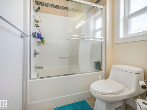 Bathroom featuring a bathtub with a sliding glass door, a toilet, and a window providing natural light - 3910 49 Avenue, Beaumont, AB - Indoor Photo Showing Bathroom