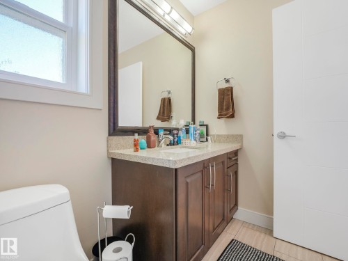 This bathroom features a contemporary vanity with a granite-style countertop, a framed mirror, and a white paneled door - 3910 49 Avenue, Beaumont, AB - Indoor Photo Showing Bathroom