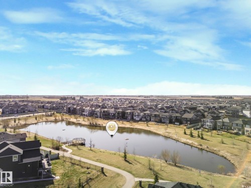 An aerial view showcasing a well-maintained pond with a wooden dock, surrounded by residential properties and green spaces - 3910 49 Avenue, Beaumont, AB - Outdoor With Body Of Water With View