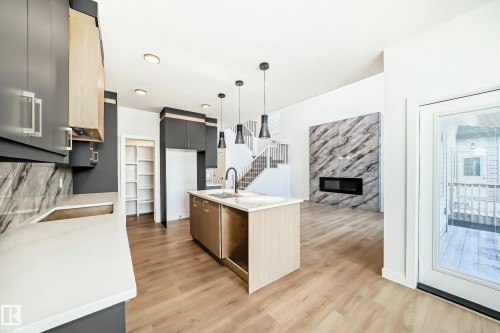The property features a contemporary kitchen with dark cabinetry, light countertops, and a central island with a sink - 341 Roberts Wynd, Leduc, AB - Indoor Photo Showing Kitchen With Fireplace