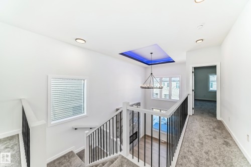 The property features a staircase with dark balusters, a chandelier, and a recessed ceiling panel with blue lighting - 341 Roberts Wynd, Leduc, AB - Indoor Photo Showing Other Room