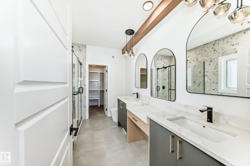 Spacious bathroom featuring dual vanities with white countertops, modern black fixtures, arched mirrors, and a walk-in shower with a glass enclosure - 341 Roberts Wynd, Leduc, AB - Indoor Photo Showing Bathroom