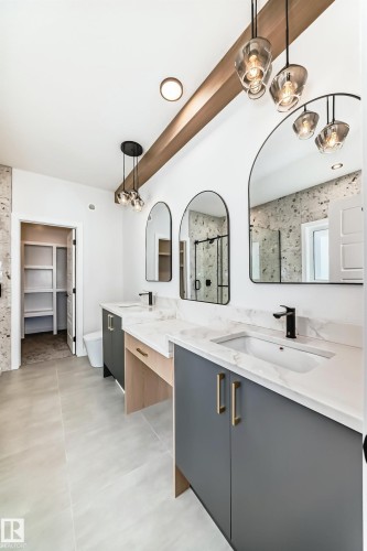 The bathroom features a double vanity with grey cabinetry, white countertops, and modern light fixtures, complemented by two arched mirrors - 341 Roberts Wynd, Leduc, AB - Indoor Photo Showing Kitchen