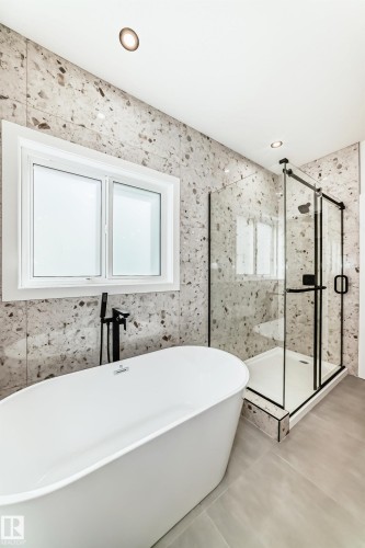 The bathroom features a freestanding soaking tub with a matte black faucet, a glass-enclosed shower with a black frame, and recessed lighting - 341 Roberts Wynd, Leduc, AB - Indoor Photo Showing Bathroom