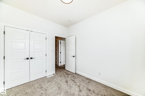 The property includes a room with light-colored carpet, white walls, and white doors with dark hardware - 341 Roberts Wynd, Leduc, AB - Indoor Photo Showing Other Room