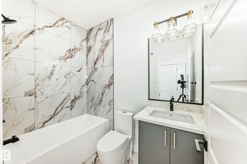 The bathroom features a modern vanity with a white countertop and dark grey cabinetry, a rectangular mirror, and a contemporary light fixture - 341 Roberts Wynd, Leduc, AB - Indoor Photo Showing Bathroom