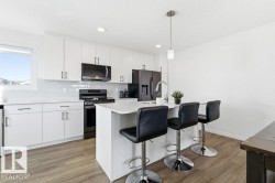 The kitchen features white cabinetry, a white subway tile backsplash, and dark stainless steel appliances - 