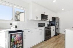 The kitchen features white cabinetry, a white subway tile backsplash, and a built-in beverage refrigerator - 