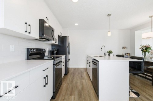 Contemporary kitchen featuring white cabinetry, black hardware, black appliances, light wood-style flooring, and an island with a sink and breakfast bar - 49 850 Secord Boulevard, Edmonton, AB - Indoor Photo Showing Kitchen With Upgraded Kitchen