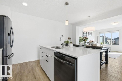 Open concept kitchen featuring a large island with a sink and dishwasher, white cabinetry, and stainless steel appliances - 49 850 Secord Boulevard, Edmonton, AB - Indoor Photo Showing Kitchen With Double Sink With Upgraded Kitchen