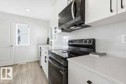 The kitchen features white cabinetry with black hardware, a subway tile backsplash, and light-colored countertops - 
