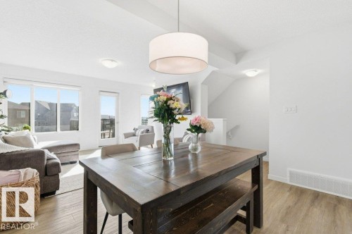 Open concept living space featuring light wood-look flooring, large windows, and a dining area with a dark wood table - 49 850 Secord Boulevard, Edmonton, AB - Indoor Photo Showing Dining Room