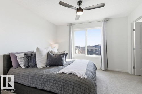This bright room features a ceiling fan, a large window with a view of residential structures, and light-colored carpeting - 49 850 Secord Boulevard, Edmonton, AB - Indoor Photo Showing Bedroom