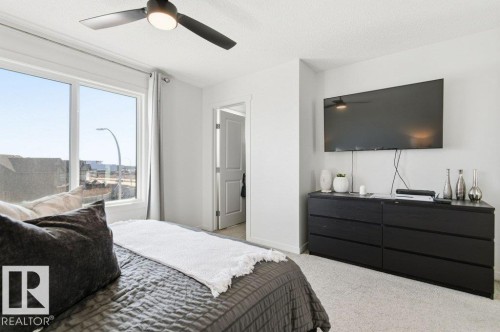 This bedroom features a ceiling fan with integrated lighting, a large window providing natural light, and light-colored carpeting - 49 850 Secord Boulevard, Edmonton, AB - Indoor Photo Showing Bedroom