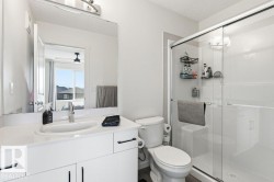 The bathroom features a modern vanity with a white countertop and an integrated sink, a toilet, and a stand-up shower with a glass enclosure - 