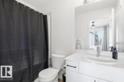 The bathroom features a vanity with a white countertop and an integrated sink, a toilet, and a shower with a dark shower curtain - 