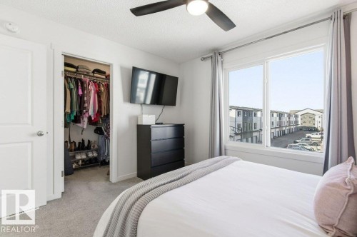 Inviting bedroom with light gray carpeting, a window offering views of the surrounding community, and a ceiling fan - 49 850 Secord Boulevard, Edmonton, AB - Indoor Photo Showing Bedroom